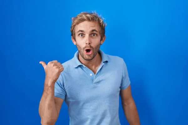 Caucasian Man Standing Blue Background Surprised Pointing Hand Finger Side — Foto Stock
