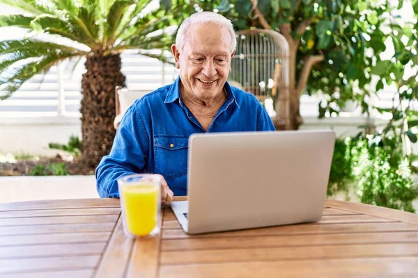 Starszy Biały Mężczyzna Pomocą Laptopa Picia Soku Pomarańczowego Siedzi Stole — Zdjęcie stockowe