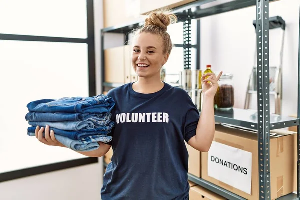 Joven Mujer Caucásica Voluntaria Sosteniendo Ropa Donada Sonriendo Feliz Señalando — Foto de Stock