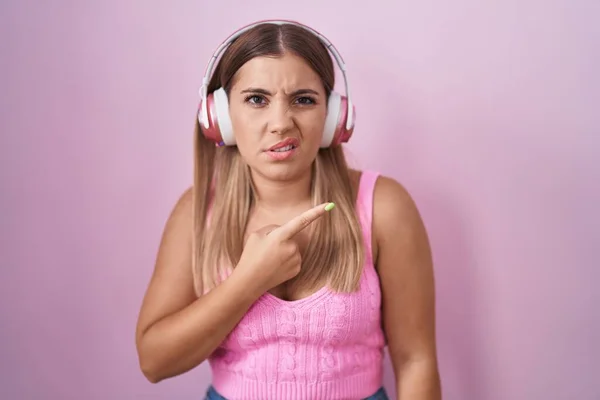 Young Blonde Woman Listening Music Using Headphones Pointing Aside Worried — Foto de Stock