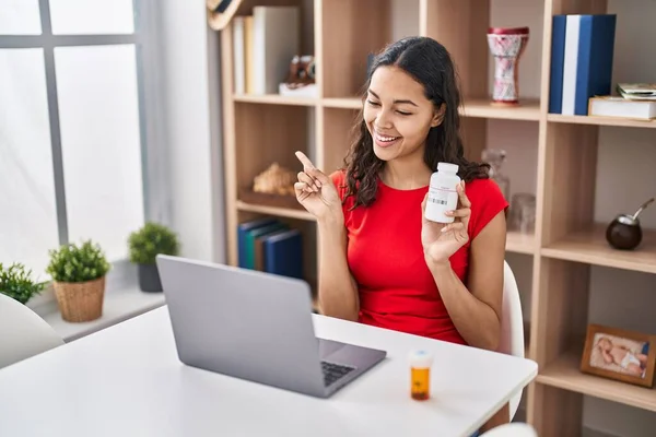 stock image Young brazilian woman doing video call showing pills to the doctor smiling happy pointing with hand and finger to the side 