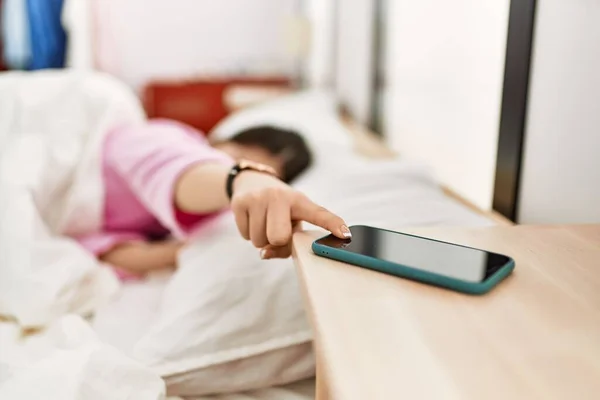 Girl turning off smartphone alarm lying on the bed at bedroom.