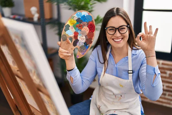 Mujer Morena Joven Sosteniendo Paleta Pintor Estudio Arte Haciendo Signo —  Fotos de Stock