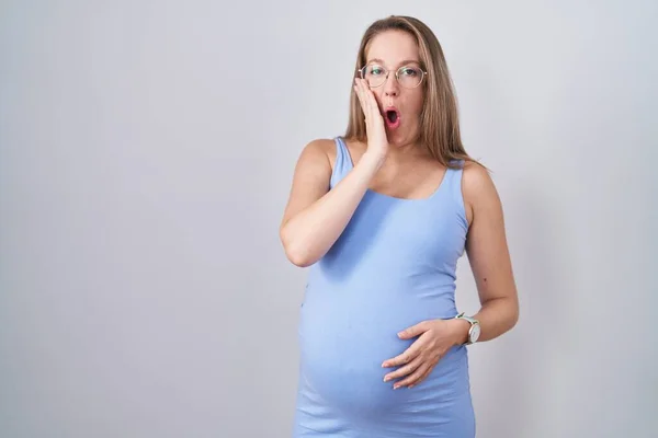若いです妊娠中の女性は白い背景を恐れてショックを受けました 驚きと驚きの表情とともに手で顔 — ストック写真