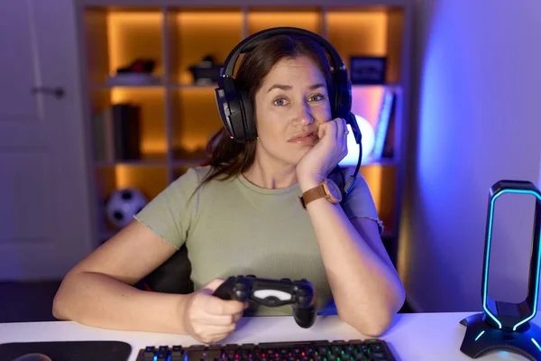 美しいブルネットの女性は 口の爪をかむ上で手でストレスと緊張を見てヘッドフォンを着てビデオゲームをしている 不安の問題 — ストック写真