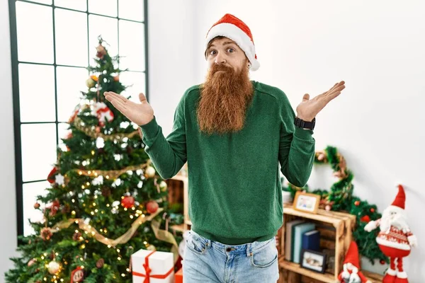 红头发男人 留着长胡子 头戴圣诞帽 头戴圣诞树 毫无头绪 满脸困惑 手臂和双手高举 怀疑概念 — 图库照片