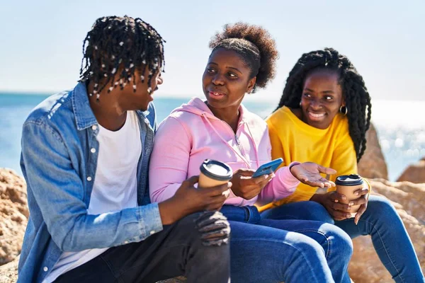 Африканские Американские Друзья Используют Смартфон Пьют Кофе Сидя Скале Берегу — стоковое фото