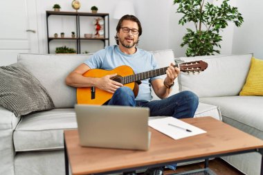 Orta yaşlı beyaz bir adam evde klasik gitar çalıyor.