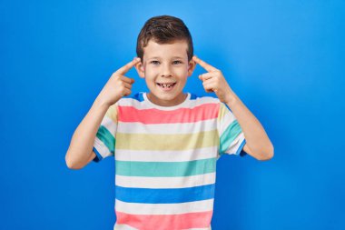 Mavi arka planda duran genç beyaz çocuk iki eliyle kafasını işaret ederek gülümsüyor, harika bir fikir ya da düşünce, iyi bir hafıza. 