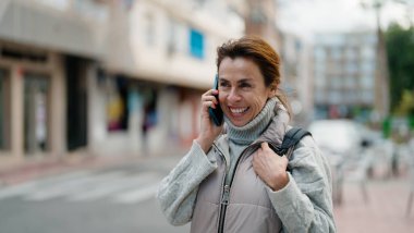 Orta yaşlı İspanyol kadın gülümsüyor. Akıllı telefondan konuşuyor.
