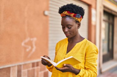 Genç Afro-Amerikalı kadın gülerek sokakta kendine güvenen kitap okuyor.