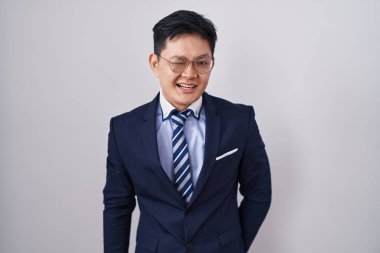 Young asian man wearing business suit and tie winking looking at the camera with sexy expression, cheerful and happy face. 