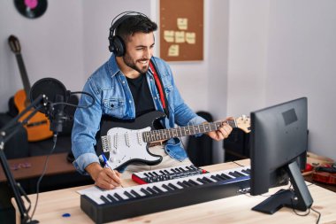 Genç İspanyol adam müzik stüdyosunda elektro gitar çalarak şarkı söylüyor.