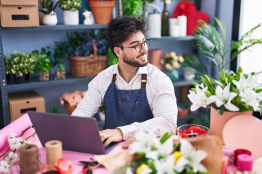 Çiçekçide dizüstü bilgisayar kullanarak gülümseyen İspanyol bir çiçekçi.