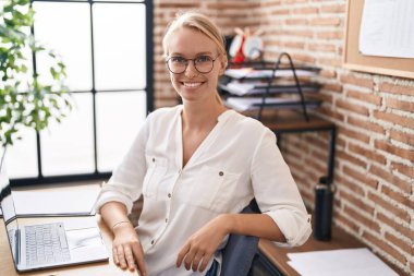 Genç sarışın iş kadını ofisteki hatırlatma kağıdına dizüstü bilgisayar kullanıyor.