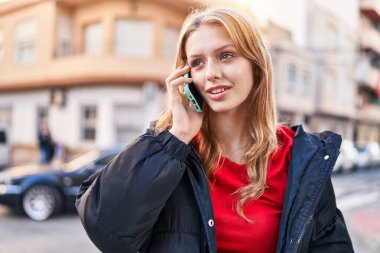 Genç sarışın kadın gülümsüyor. Kendine güveni tam. Akıllı telefondan konuşuyor.