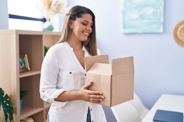 Young hispanic woman smiling confident holding cardboard box at home