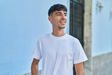 Young hispanic man smiling confident looking to the side at street