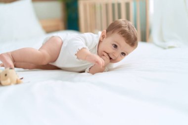 Sevimli çocuk yatakta oyuncak ayıyla yatıyor. Yatak odasında ciddi bir ifadesi var.