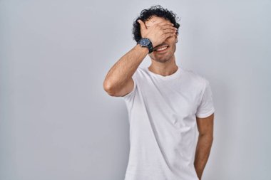 Soyutlanmış arka planda dikilen İspanyol bir adam. Gülümsüyor ve gülümsüyor. Gözlerini şaşkınlıkla kapatıyor. kör kavram. 