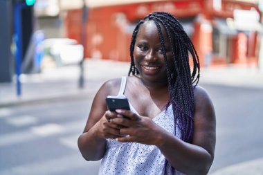 Afro-Amerikalı kadın sokakta akıllı telefon kullanarak kendine güveniyor.