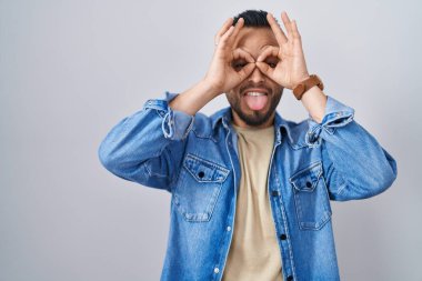 Tecrit edilmiş arka planda duran genç bir İspanyol dürbün gibi jest yapıyor, gözleri parmaklarından bakıyor. çılgın ifade. 