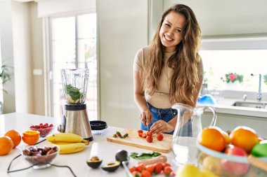 Genç ve güzel İspanyol kadın mutfakta çilek doğrayan blender ile sebze suyu hazırlıyor.