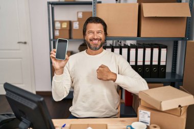 Küçük işletme şirketinde çalışan yakışıklı orta yaşlı bir adam elinde akıllı bir telefonla mutlu ve gururlu bir kendini işaret ediyor. 