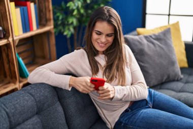 Evdeki kanepede oturan akıllı telefon kullanan genç, güzel İspanyol kadın.