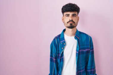 Pembe arka planda duran sakallı İspanyol genç adam yüzünde ciddi bir ifadeyle rahatlamış. Basit ve doğal bir şekilde kameraya bakıyorsun.. 