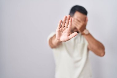 Hispanic man with beard standing over isolated background covering eyes with hands and doing stop gesture with sad and fear expression. embarrassed and negative concept. 