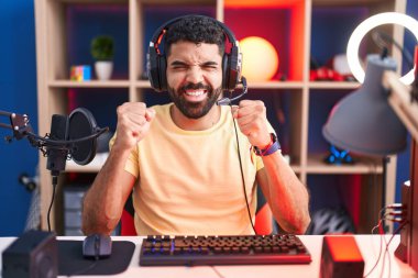 Hispanic man with beard playing video games with headphones excited for success with arms raised and eyes closed celebrating victory smiling. winner concept. 