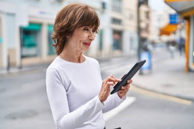 Sokakta dokunmatik ped kullanan orta yaşlı bir kadın gülümsüyor.