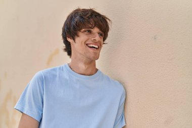 Sarışın genç adam gülümsüyor. Kendinden emin. Caddenin kenarına bakıyor.