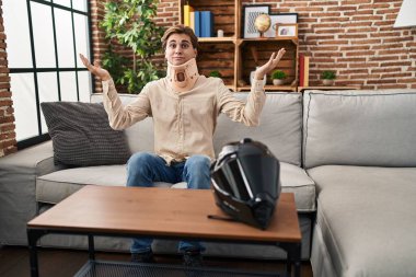 Young man wearing cervical collar for motorbike accident clueless and confused expression with arms and hands raised. doubt concept. 