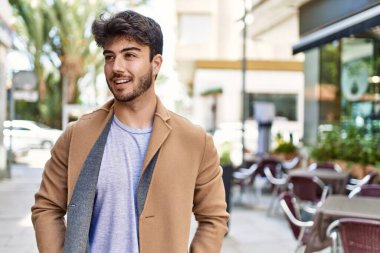 Genç İspanyol adam gülümseyerek şehirde mutlu mesut dikiliyor..