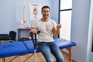 Rehabilitasyon kliniğinde koltuk değneği takmış sakallı genç İspanyol adam gururla bağırıyor, zaferi kutluyor ve başarıyı kollarını kaldırarak kutluyor. 