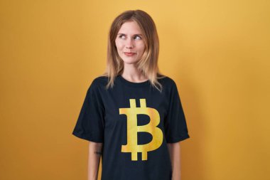 Sarışın, beyaz kadın bitcoin tişört giyiyor. Gülümsüyor, yan tarafa bakıyor ve düşünüyor.. 