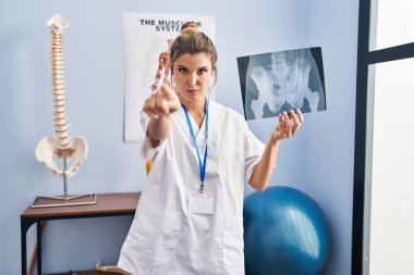 Elinde leğen kemiği radyografisi olan genç bir kadın kamerayı ve seni işaret ediyor. Kendine güvenen bir jest, ciddi görünüyor. 