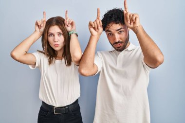 Genç bir çift, sıradan kıyafetler giyip birlikte komik hareketler yapıyorlar. Parmakları başlarının üstünde boğa boynuzu gibi. 