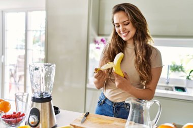 Genç, güzel İspanyol kadın mutfakta muz soyan blender ile sebze suyu hazırlıyor.
