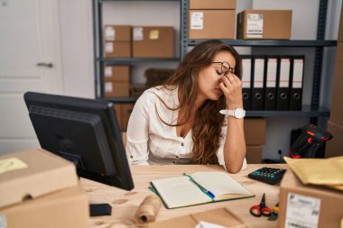 Young hispanic woman working at small business ecommerce tired rubbing nose and eyes feeling fatigue and headache. stress and frustration concept. 