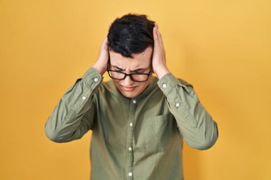 Non binary person standing over yellow background suffering from headache desperate and stressed because pain and migraine. hands on head. 