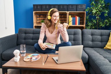 Genç ve güzel bir kadın resim yapıyor. İnternetten öğretmenlere bakıyor. Başparmağını kaldırıyor ve ağzı açık gülümsüyor. 