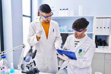 Laboratuvarda çalışan iki bilim adamı test tüpleri tutuyor.