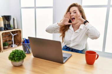 Young caucasian woman working at the office using computer laptop smiling cheerful playing peek a boo with hands showing face. surprised and exited 