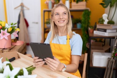 Young blonde woman florist smiling confident using touchpad at flower shop