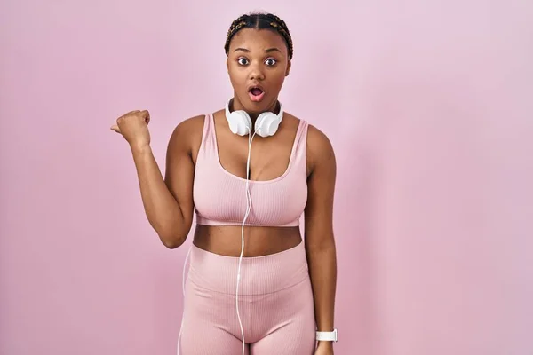 African American Woman Braids Wearing Sportswear Headphones Surprised Pointing Hand — Stockfoto