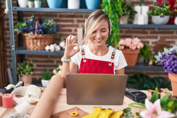Young blonde woman working at florist shop doing video call doing ok sign with fingers, smiling friendly gesturing excellent symbol