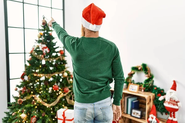 红头发的男人 留着长长的胡子 头戴圣诞礼帽 头戴圣诞礼帽 头戴圣诞礼帽 头戴圣诞礼帽 背对着圣诞树 手拿着手指朝前看 — 图库照片